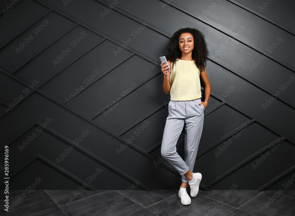 Portrait of beautiful African-American woman with mobile phone near dark wall