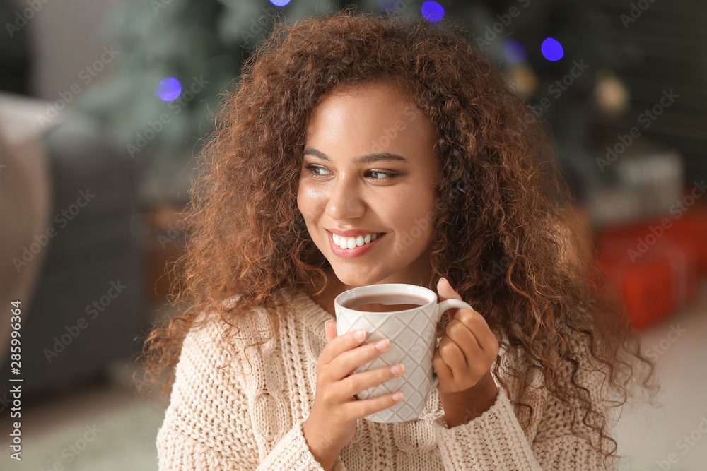 Young African-American woman drinking hot chocolate at home on Christmas eve