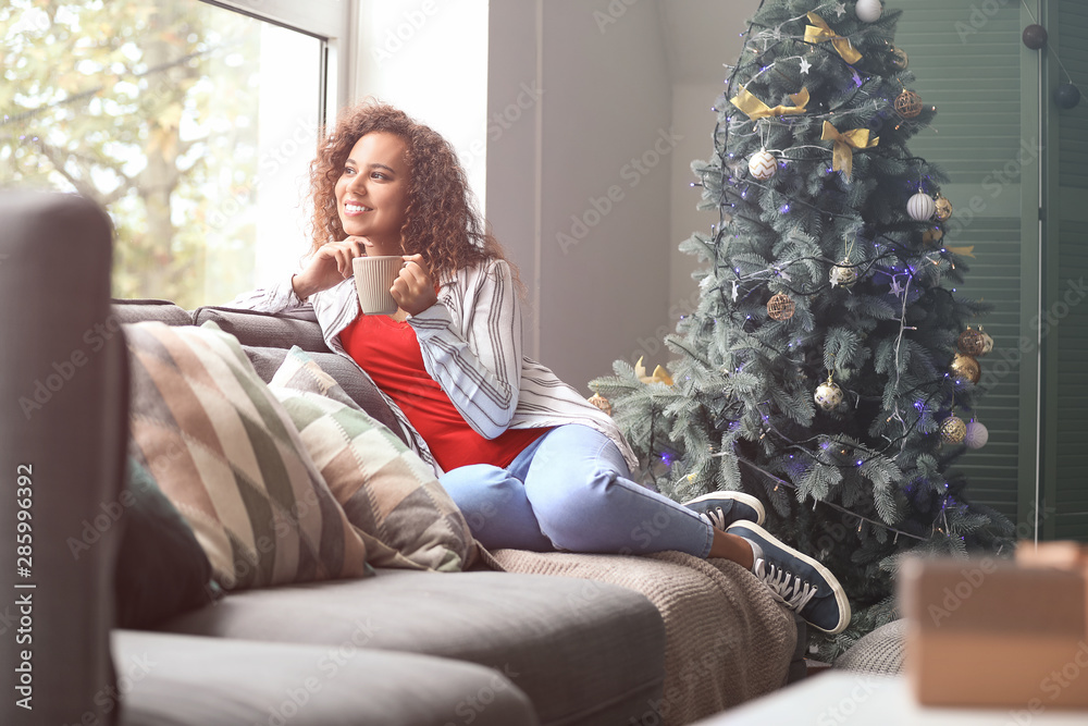 Young African-American woman drinking hot chocolate at home on Christmas eve