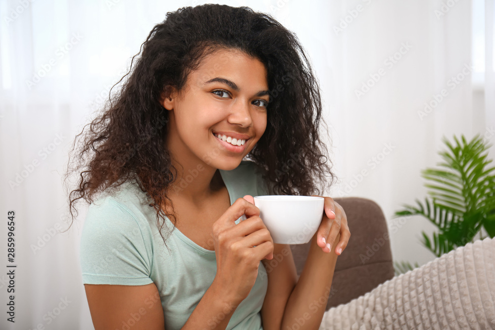 Beautiful young African-American woman drinking coffee at home