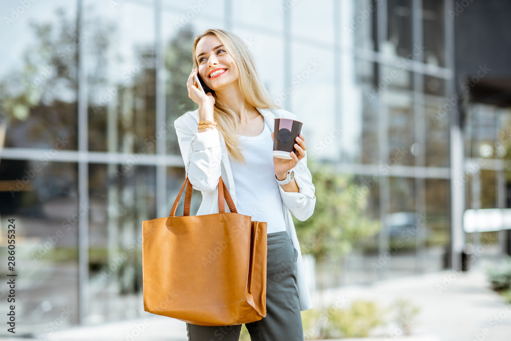 Portrait of a young businesswoman talking with phone during a coffee break near the office building 