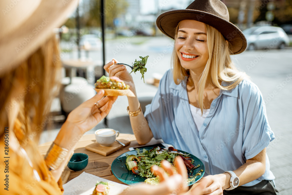 Two female best friends eating healthy food while sitting together on a restaurant terrace on a summ