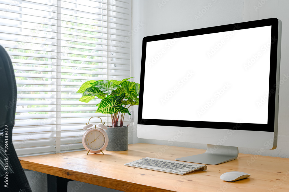 workspace with computer with blank white screen, and office supplies on a wooden desk