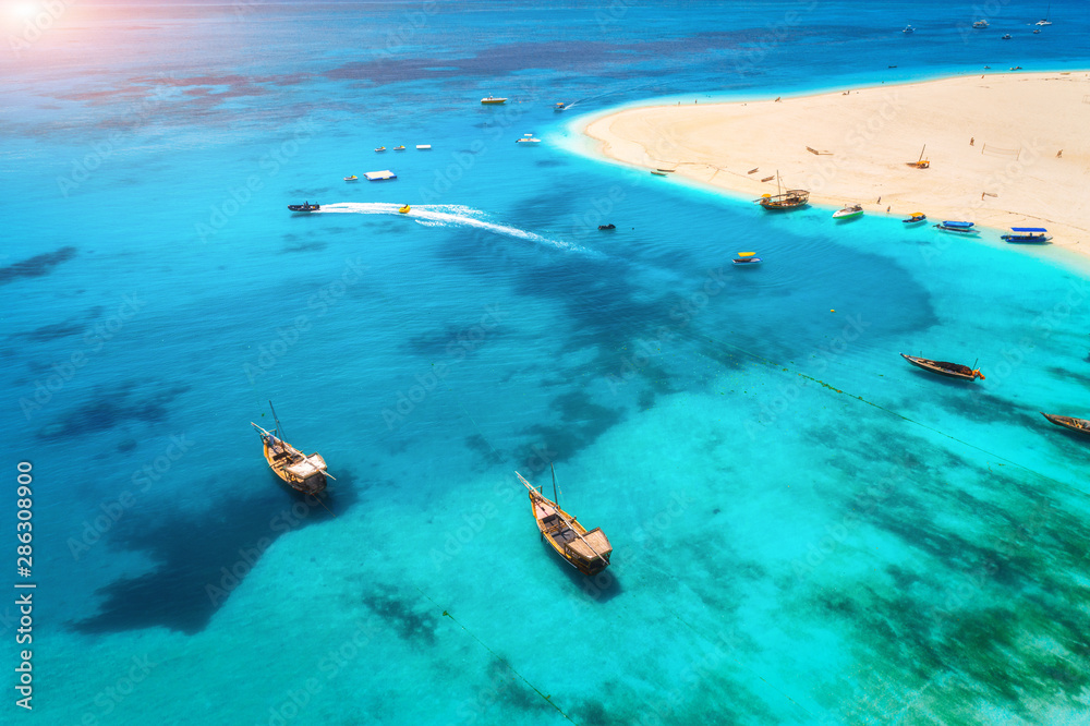 Aerial view of fishing boats and yachts on tropical sea coast with white sandy beach at summer eveni