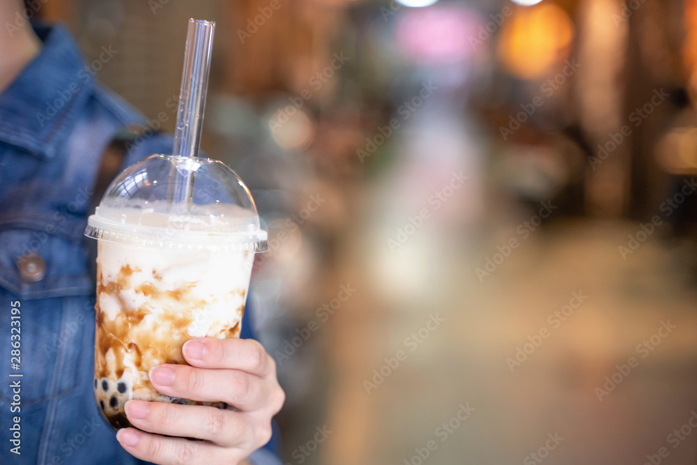 穿着牛仔夹克的年轻女孩正在用杯子喝红糖口味的木薯珍珠泡奶茶