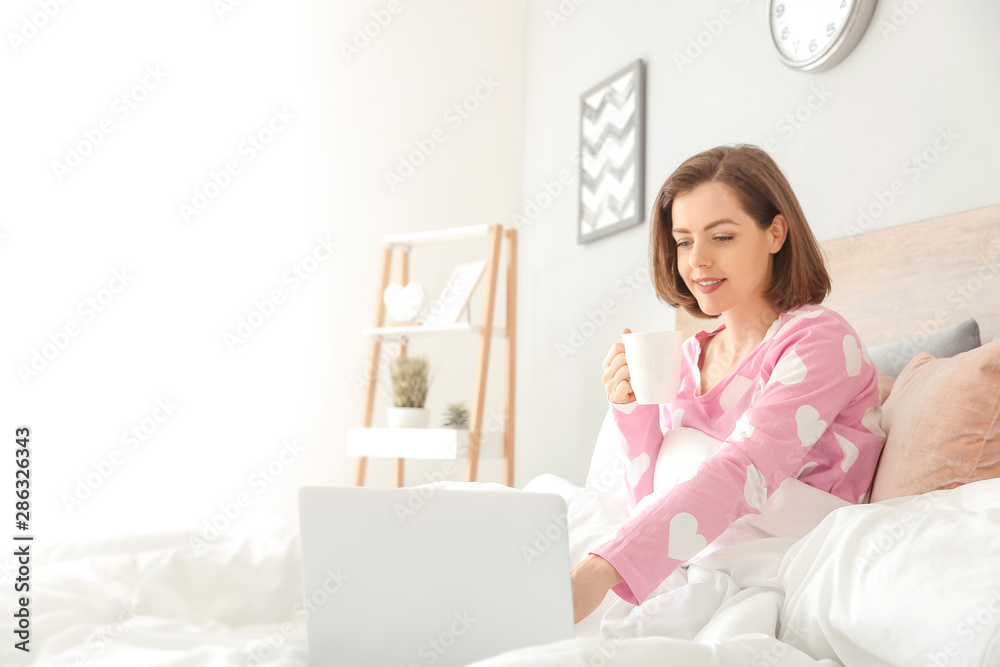 Morning of beautiful young woman with laptop drinking coffee in bed