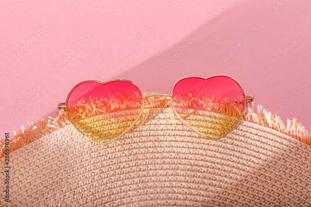 Stylish sunglasses with straw hat on color background