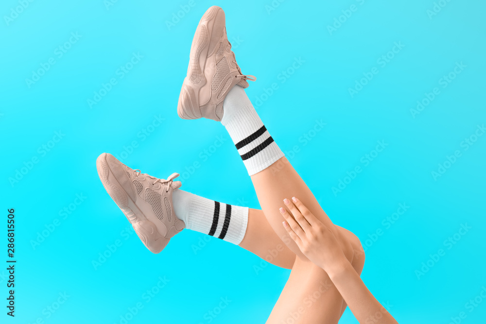 Stylish young woman in shoes and socks on color background