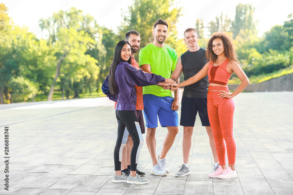 Group of young sporty people putting hands together outdoors