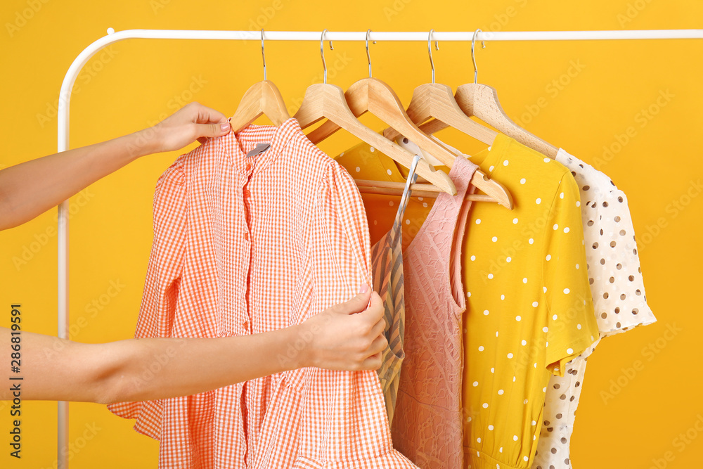 Woman choosing clothes hanging on rack against color background