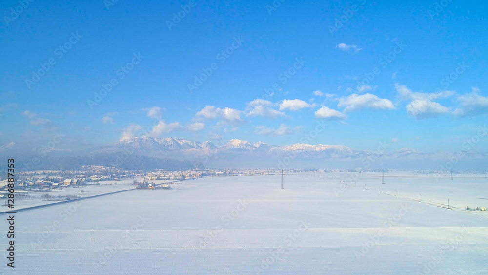 空中飞行：在冬天的早晨，在白色的雪地上飞向岩石山脉