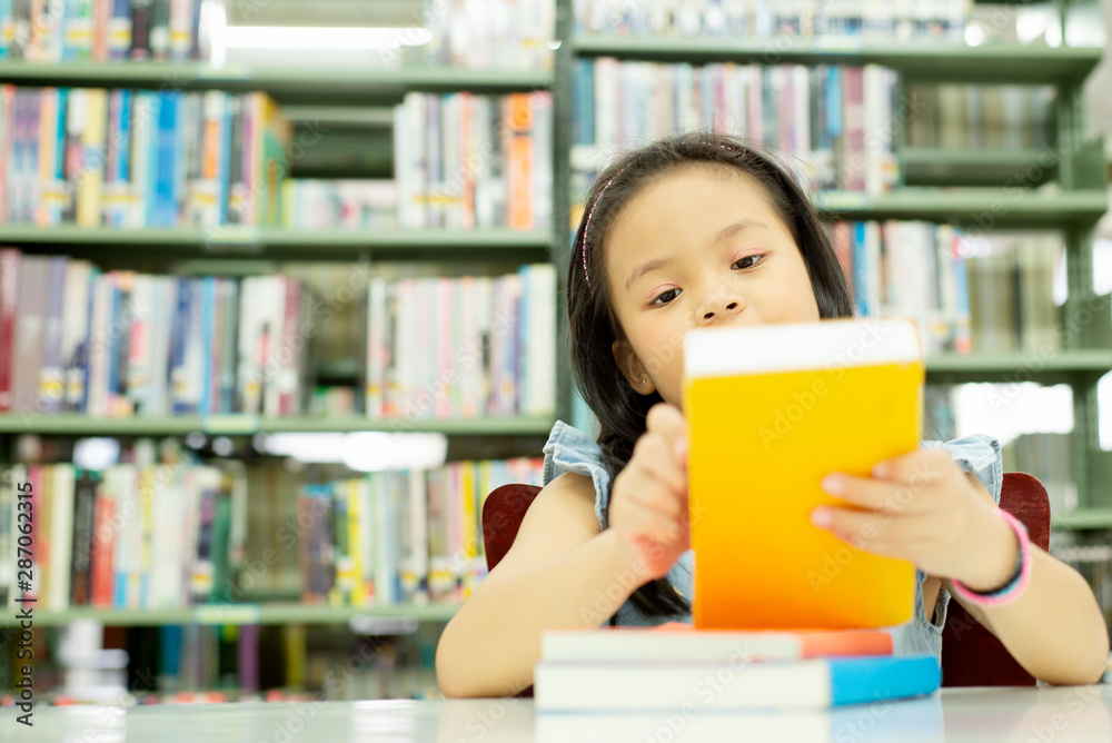 微笑可爱的亚洲小女孩坐在学校图书馆看书的肖像，教育