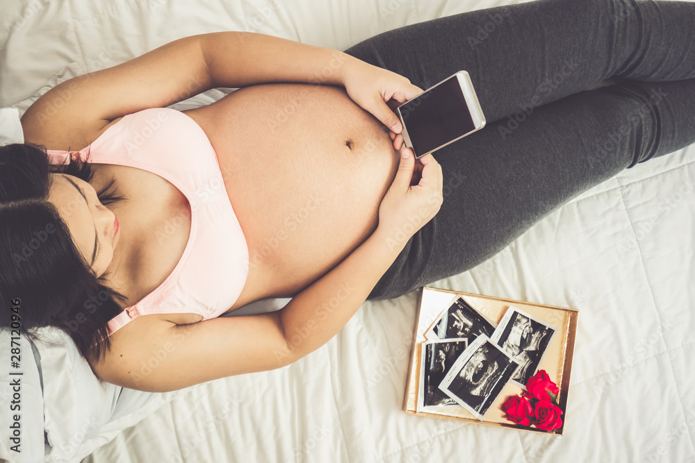 Pregnant woman feeling happy at home while taking care of her child. The young expecting mother hold