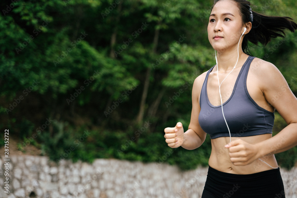 年轻的亚洲女性在绿色乡村跑步。女孩在自然森林公园慢跑