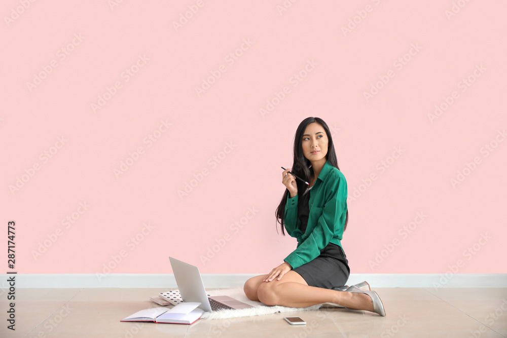 Young Asian blogger with laptop sitting near color wall