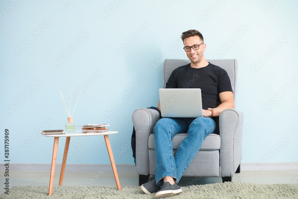 Male blogger with laptop sitting in armchair near color wall