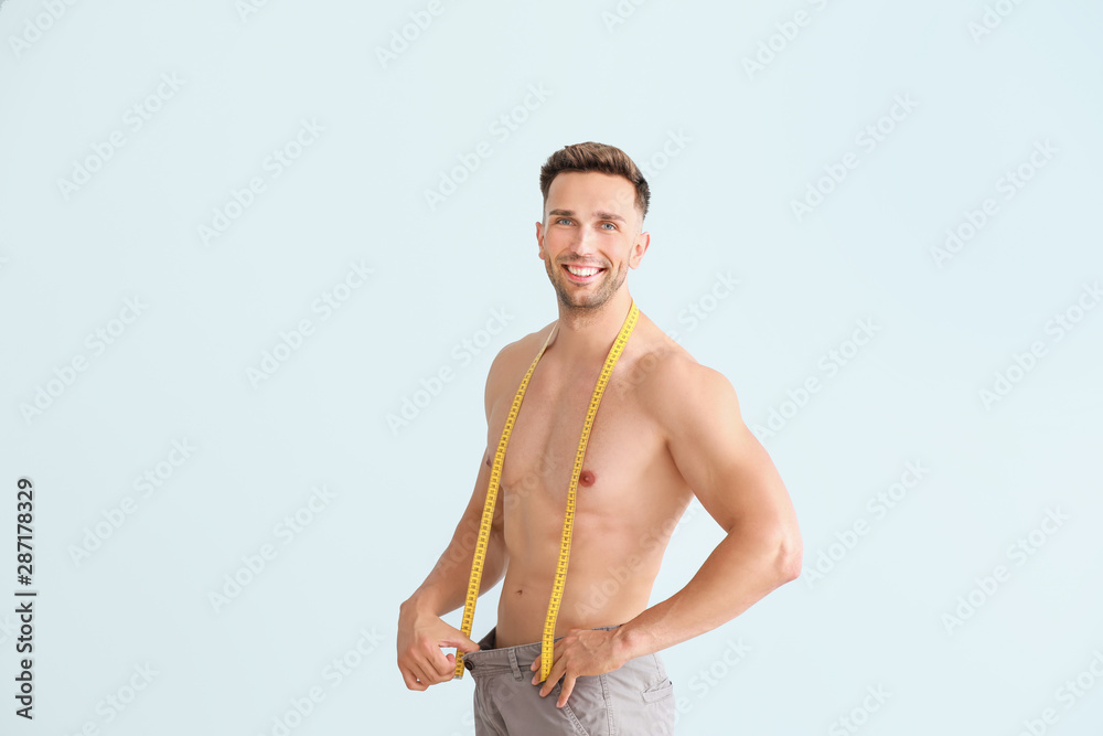 Handsome muscular man in loose pants and with measuring tape on color background. Weight loss concep