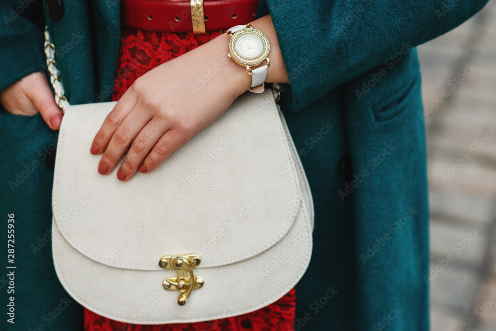 Street fashion details: crop of white luxury woman`s wrist watch on hand, snakeskin textured small b