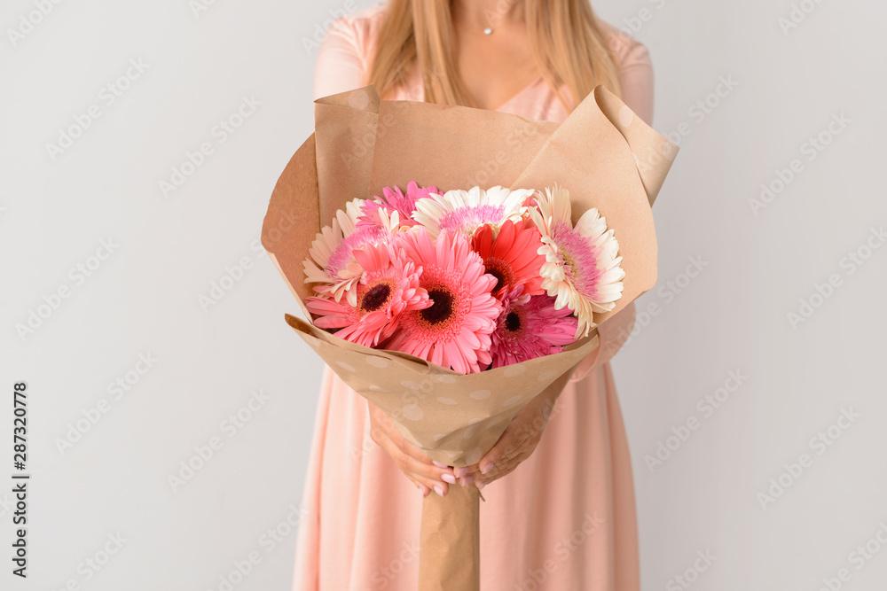 Woman with bouquet of beautiful gerbera flowers on light background