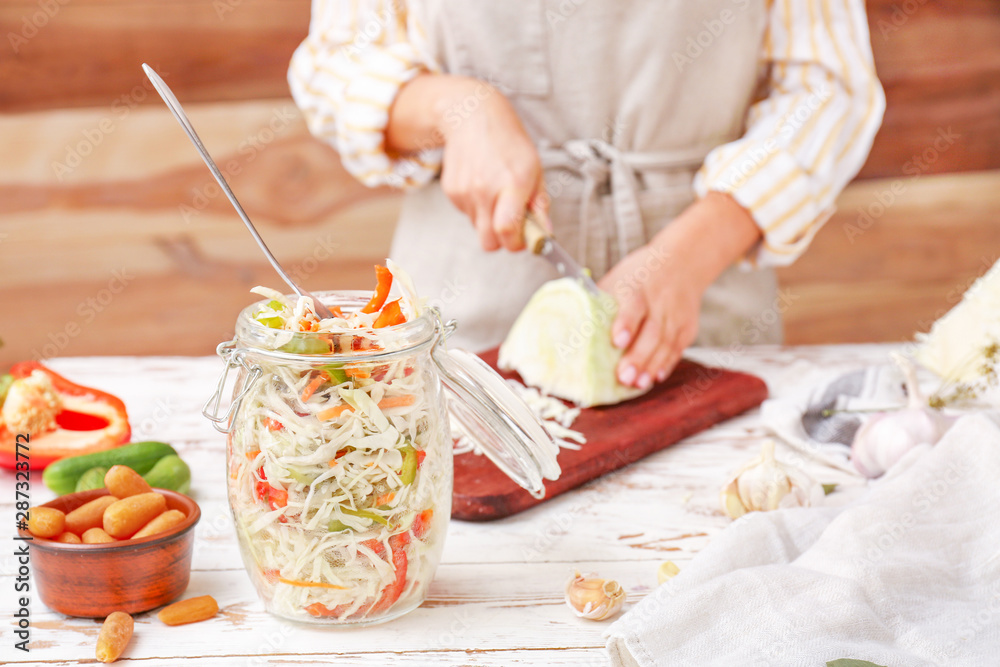 Woman preparing cabbage for fermentation at table, closeup