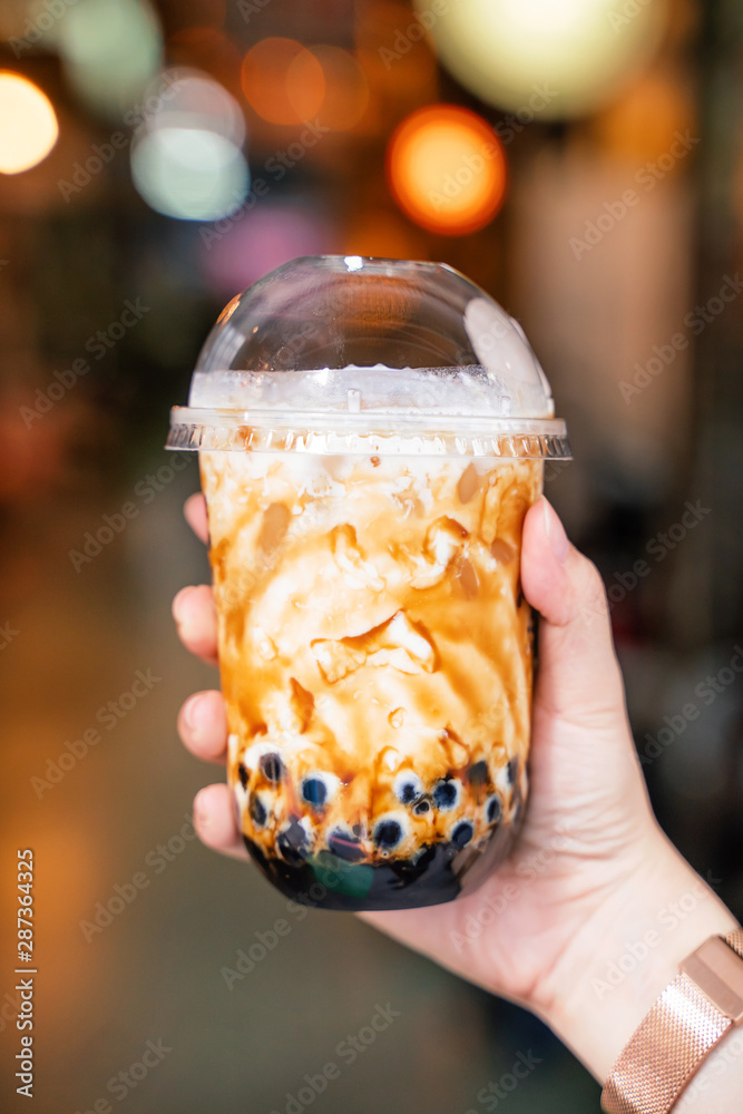 Young girl is holding and showing a cup of brown sugar flavored tapioca pearl bubble milk tea in nig