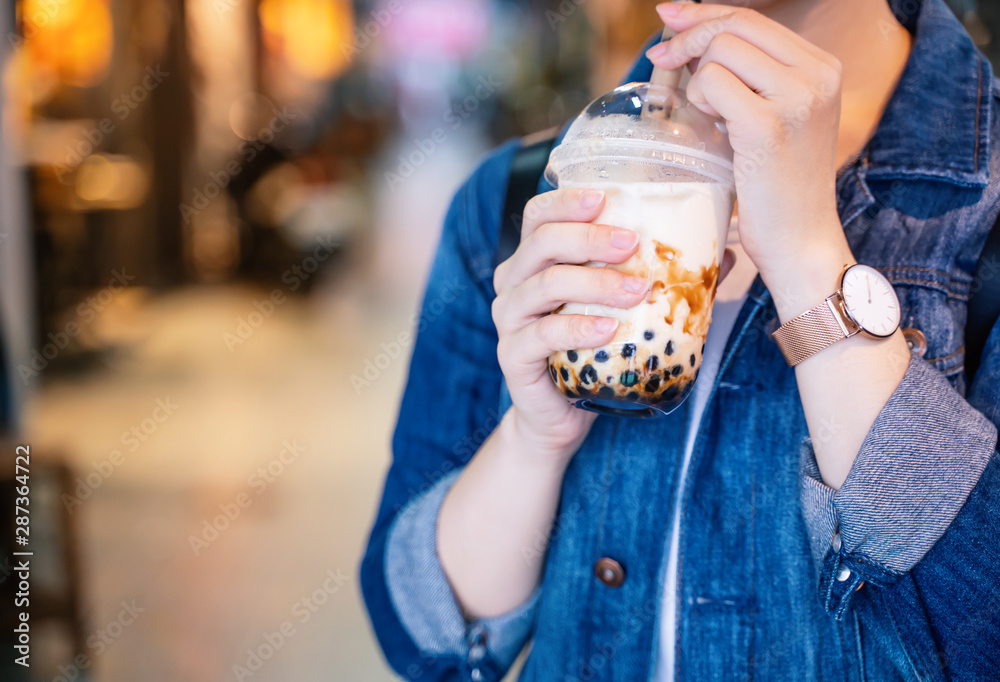 穿着牛仔夹克的年轻女孩正在用杯子喝红糖口味的木薯珍珠泡奶茶