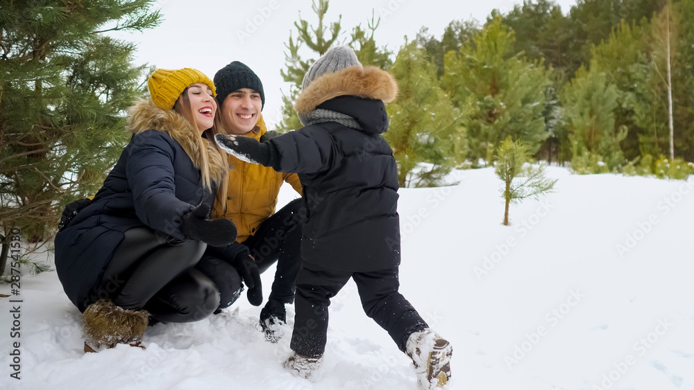 儿子在冬天的公园里跑步，拥抱着他的父母。他们一起在雪中飘落。家庭快乐