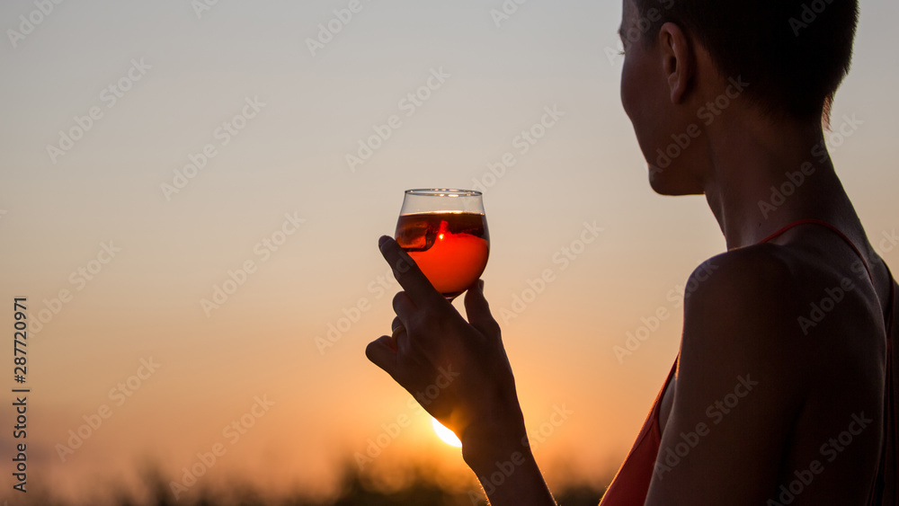 Happy brunette woman holding orange cocktail over sunset sky in orange colors