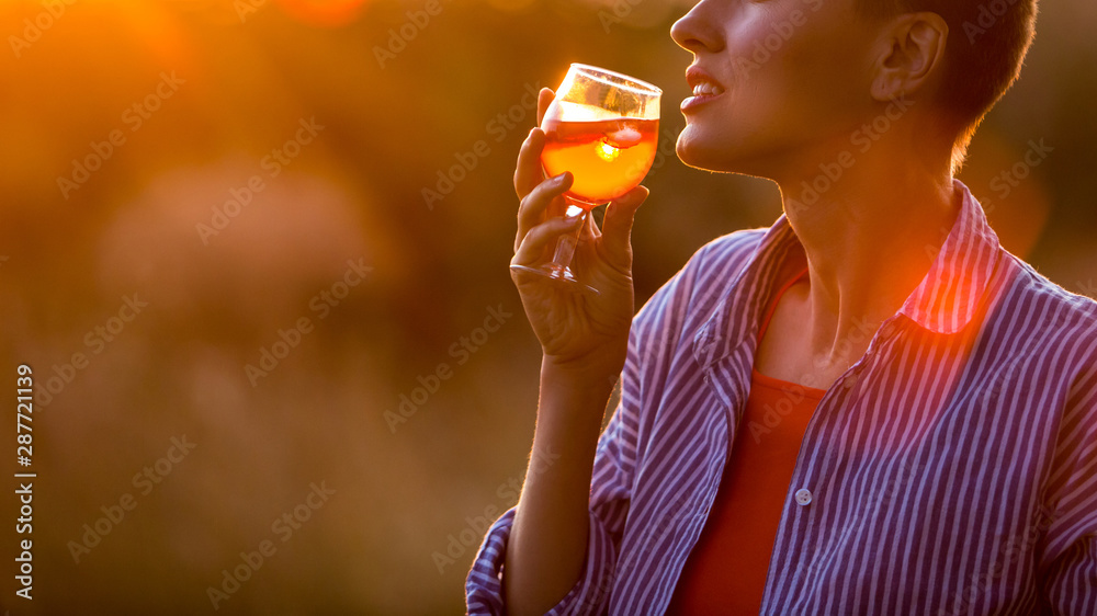 快乐的深色女人在日落的天空中拿着橙色的鸡尾酒