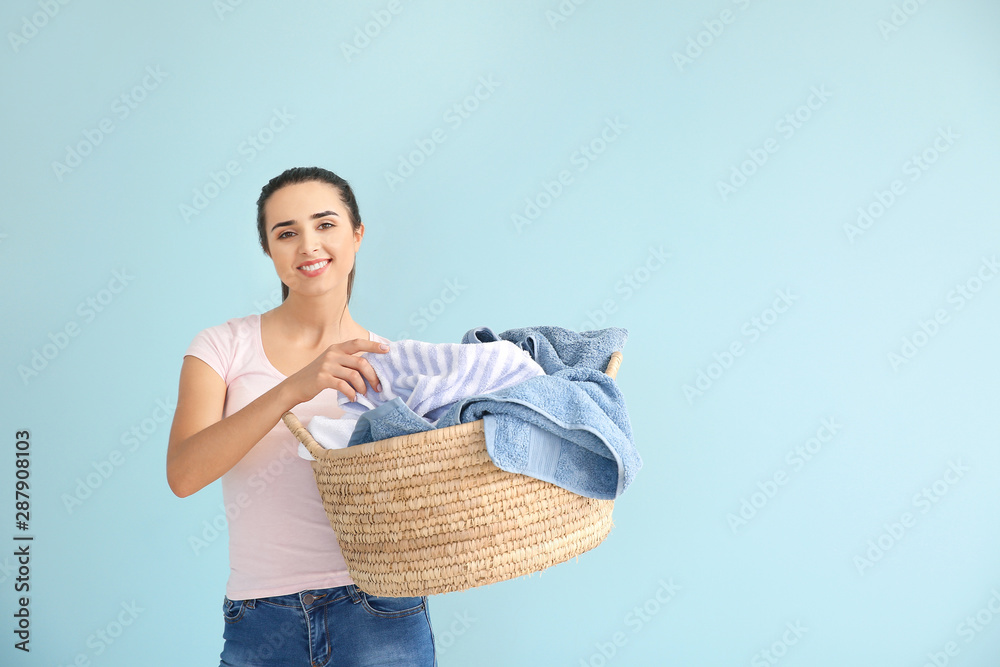 Beautiful young woman with laundry on color background