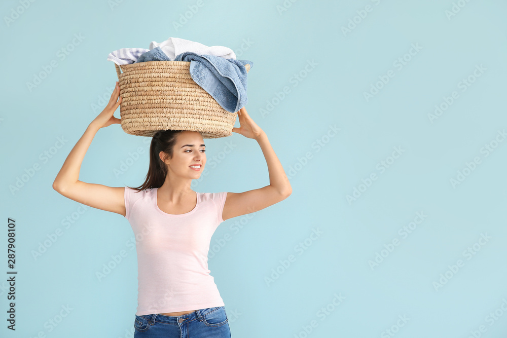 Beautiful young woman with basket of laundry on color background