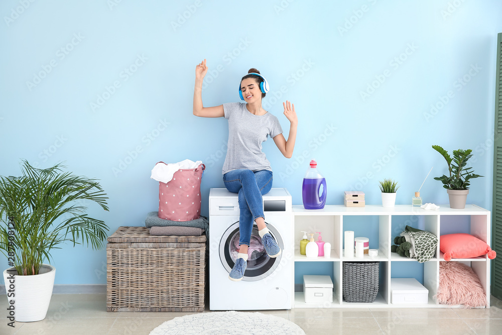 Beautiful young woman listening to music while doing laundry at home