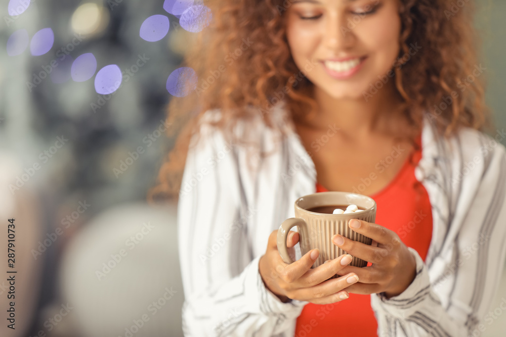 Young African-American woman drinking hot chocolate at home on Christmas eve