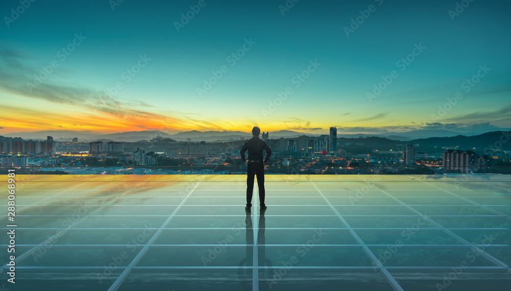 Businessman standing at transparent glass floor on rooftop with city skyline, success and thinking c