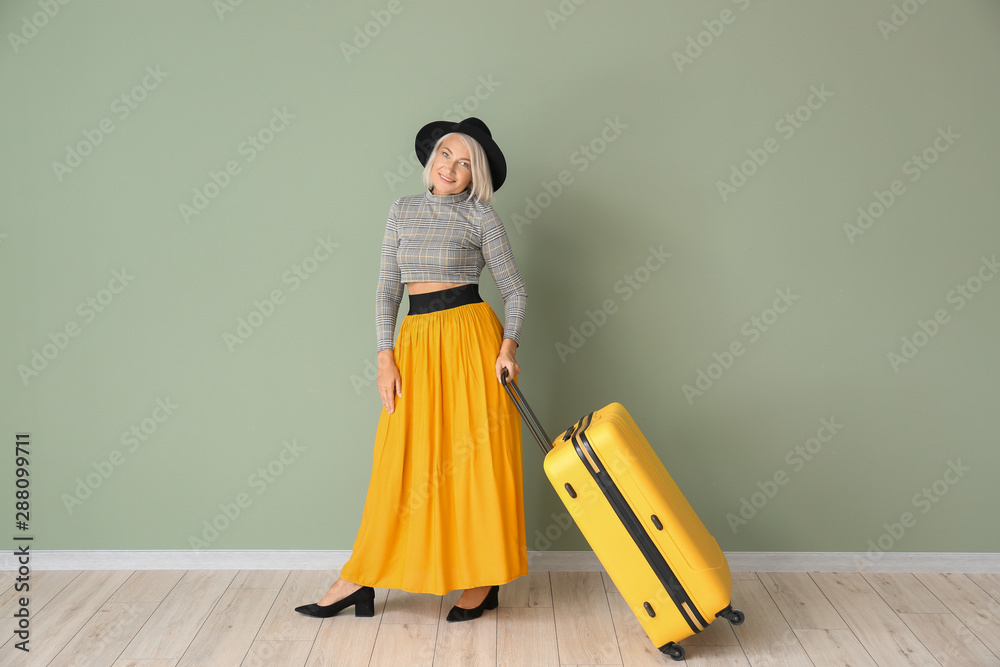 Mature woman with luggage against color wall