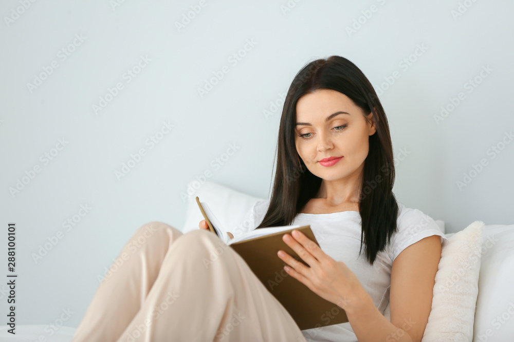 Beautiful young woman reading book in bedroom