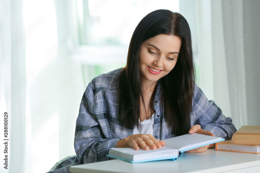 Beautiful young woman reading book at home