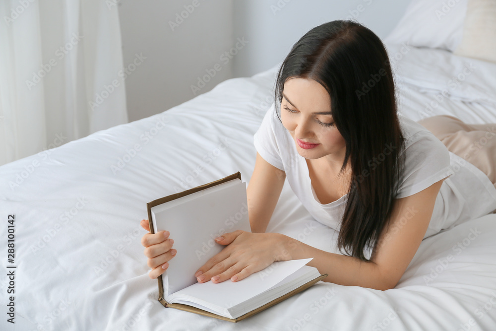 Beautiful young woman reading book in bedroom