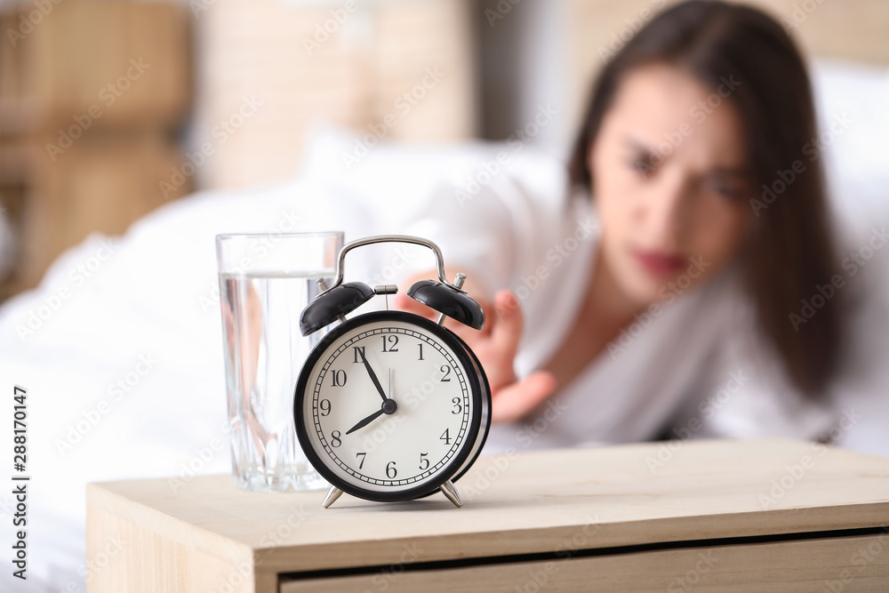 Sleepy young woman turning off alarm clock in morning