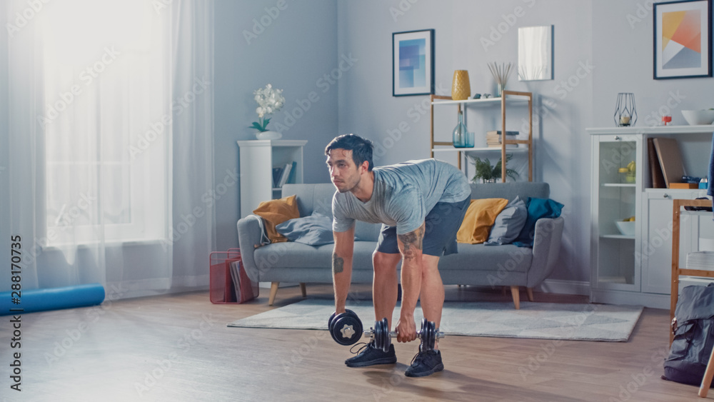 Muscular Athletic Fit Man in T-shirt and Shorts is Doing Exercises with Dumbbells at Home in His Spa