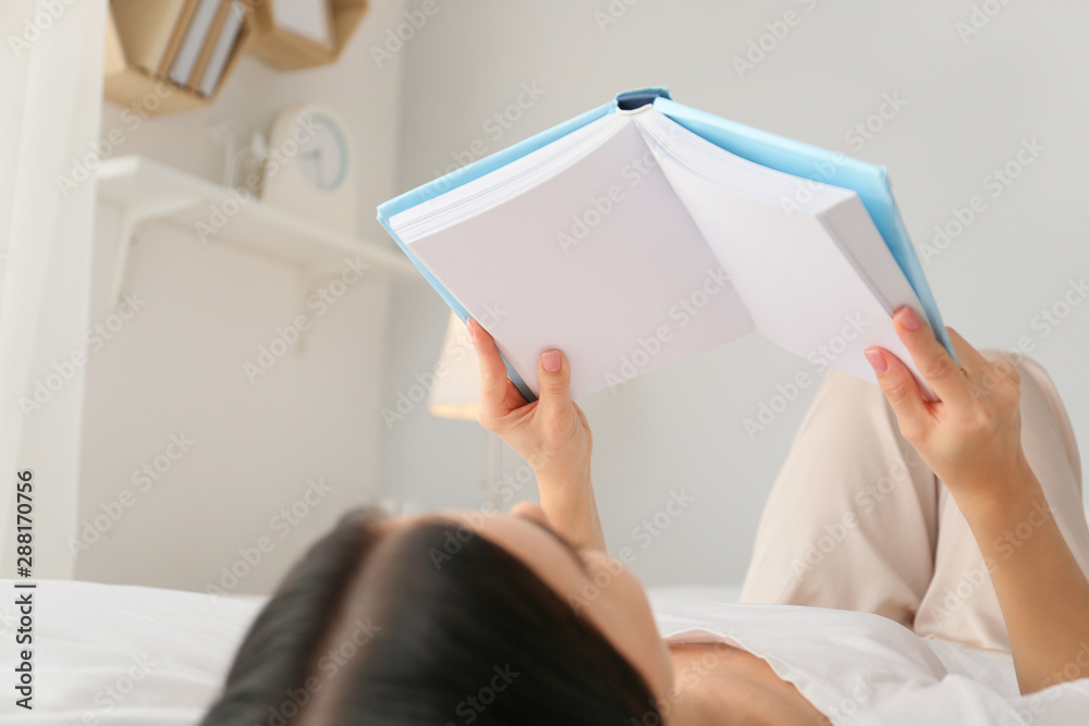 Beautiful young woman reading book in bedroom