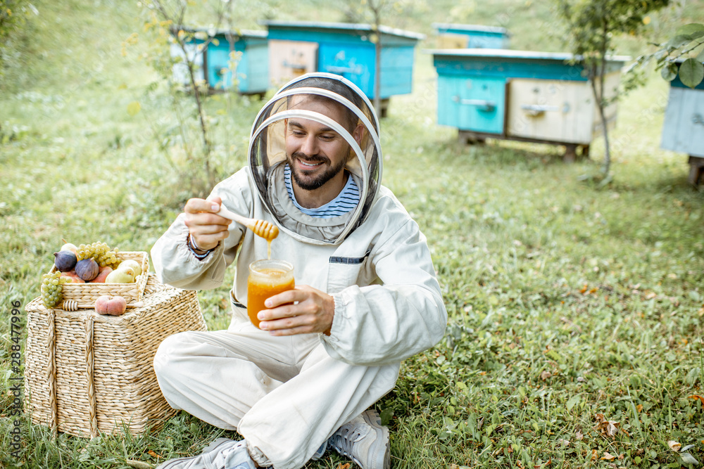 Portrait of a cheerful beekeeper in protective uniform with honey products and sweet fruits on the a