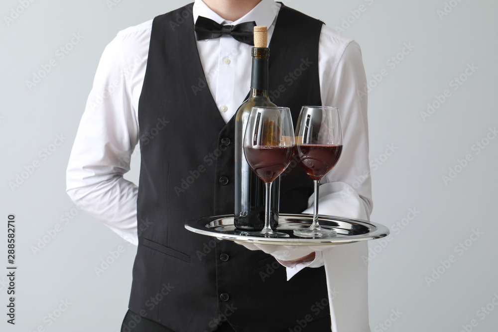 Handsome waiter with wine on light background