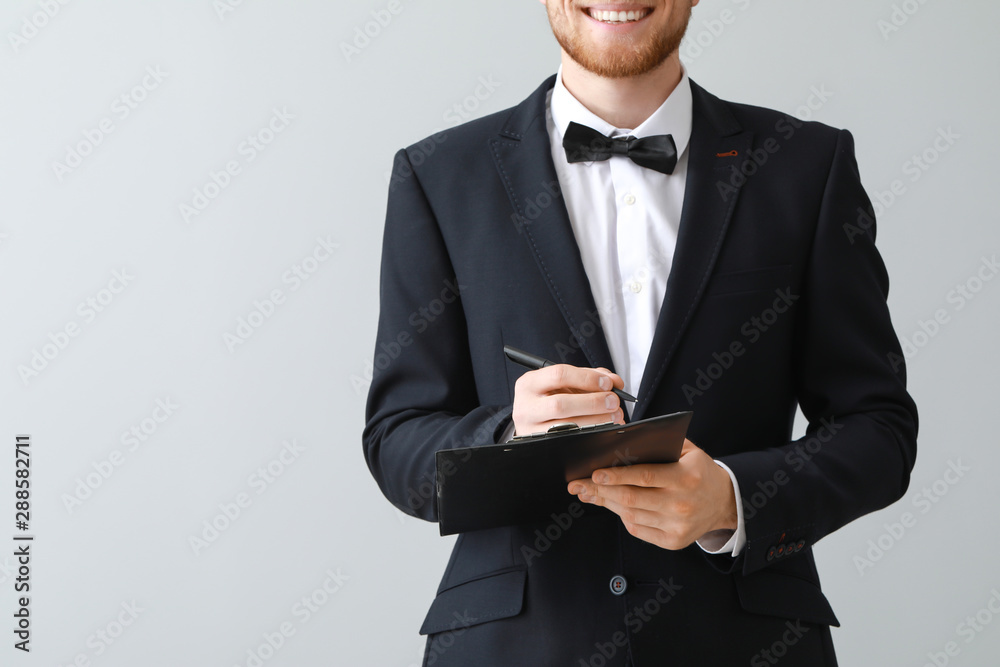 Handsome waiter with clipboard on light background