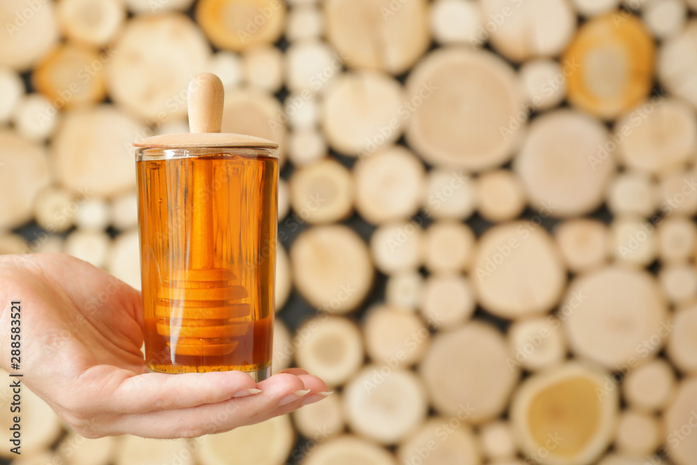 Female hand with glass of sweet honey on wooden background