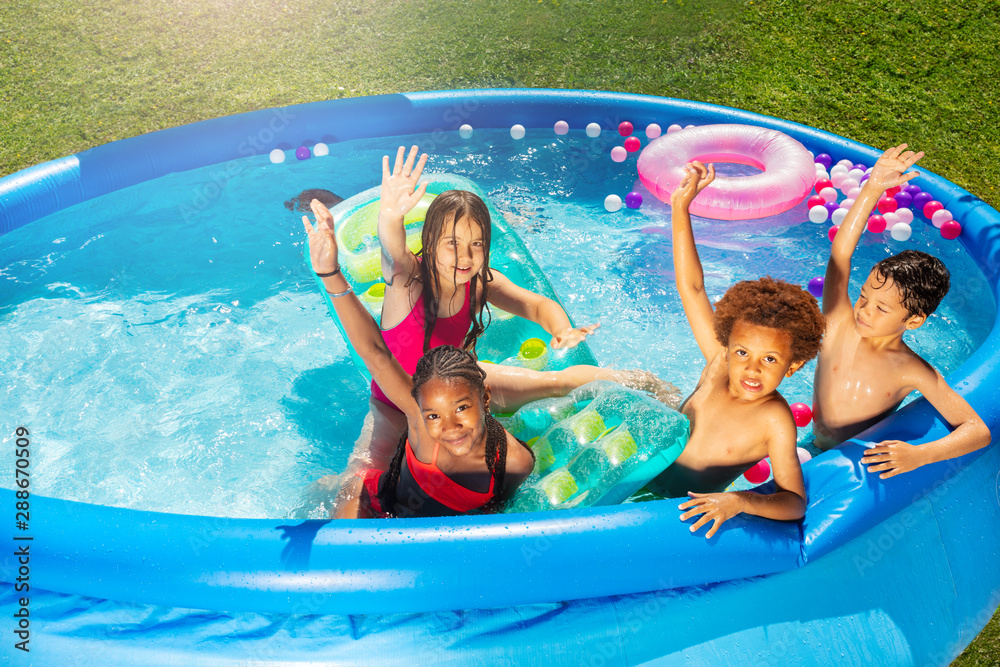 Group of kids play in swimming pool lifting hands