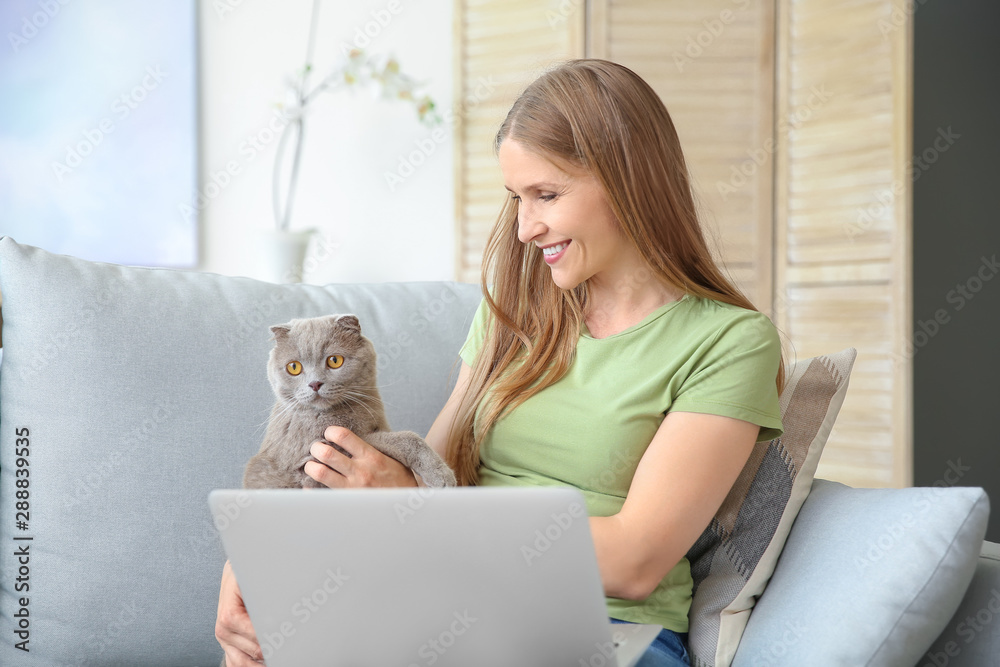 Beautiful woman with cute cat and laptop sitting on sofa at home