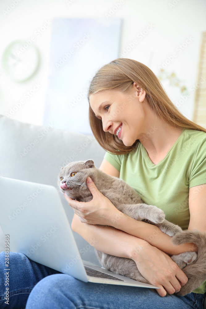 Beautiful woman with cute cat and laptop sitting on sofa at home