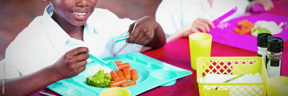 Boy and girl in school uniforms having lunch in school cafeteria