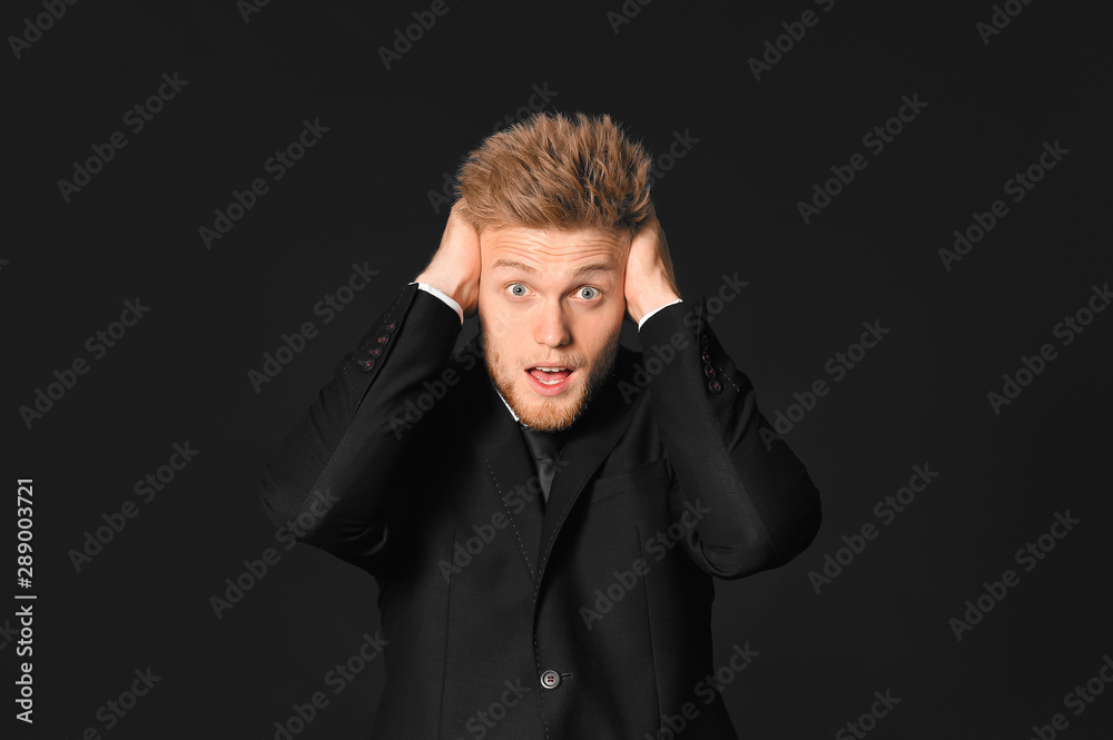 Shocked young businessman on dark background